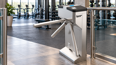 FERN360 tripod turnstile installed at the entrance of a modern commercial gym with fitness equipment in the background.