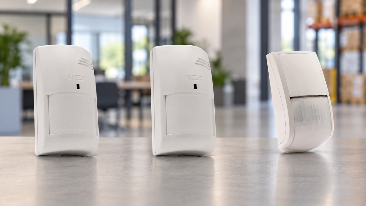 Three commercial alarm motion detectors against a blurred office and warehouse background.