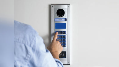 Visitor using a stainless-steel video intercom with camera, keypad and RFID access reader at an apartment building entrance in NZ
