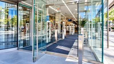 Modern commercial glass entrance with swing doors and an accessibility control, illustrating automatic door access for NZ businesses.